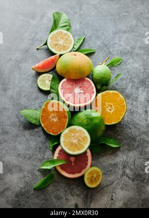 From above heap of slices and halves of limes with grapefruits and oranges served on gray background in light studio Stock Photo