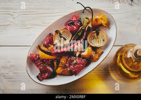 Top view of assorted grilled vegetables served on oval plate near bottle of olive oil on wooden table Stock Photo