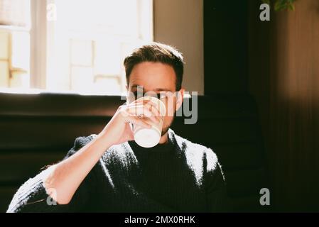 Man drinking coffee in a paper cup inside a coffee shop Stock Photo