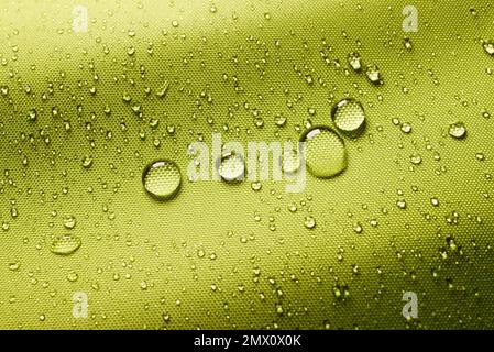 Top view closeup of green background with small round drops of water on textured waterproof impregnated fabric in light room Stock Photo