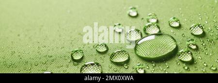 Background closeup of small round transparent clean drops on wet protective green waterproof impregnated textile with various small water drops Stock Photo