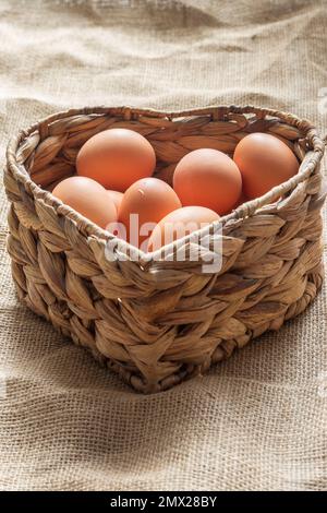 Free range chicken eggs in a heart shaped water hyacinth wicker basket. On a hessian sack cloth background Stock Photo
