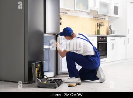 Male technician with screwdriver repairing refrigerator in kitchen Stock Photo