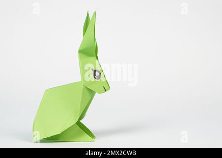 A green origami rabbit on a white background. Crafts for Easter, fold from paper, do it yourself, place for text. Stock Photo