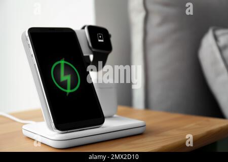 Smartphone, watch and earphones charging on wireless pad in room. Space for text Stock Photo