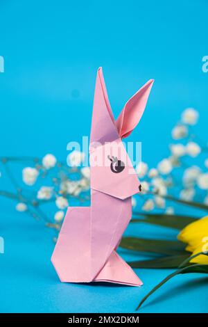 A pink and yellow origami rabbits on a blue background. Crafts for ...