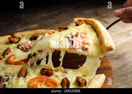 Woman taking piece of delicious seafood pizza at wooden table, closeup Stock Photo