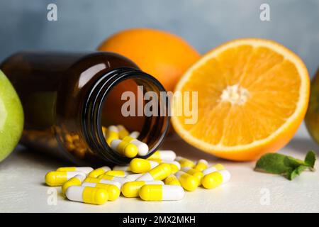Bottle with vitamin pills and fruits on white table, closeup Stock Photo