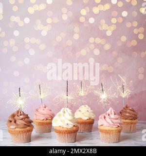 Birthday cupcakes with sparklers on table against light pink background Stock Photo