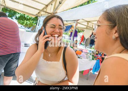 Latino adult happy woman of Venezuelan ethnicity dressed in white and glasses standing at a craft fair, talking on the phone with her eyes closed and Stock Photo
