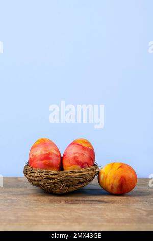 Three Easter eggs in a decorative nest of sisal on a wooden background. Happy Easter concept. Greeting card. Stock Photo