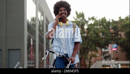 Young african american man talking on smart phone in the street with urban bike. Young digital entrepreneurs Stock Photo