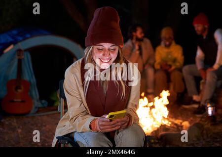 Caucasian woman sitting outside in a camping using phone to be connected and sending messages happy. Stock Photo
