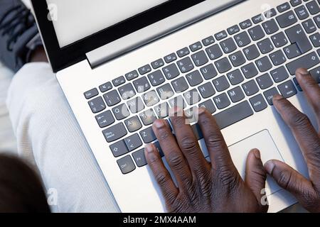 Close up african black hands typing on laptop computer keyboard on legs. Businessman response to email, online purchase. Work and social integration. Stock Photo