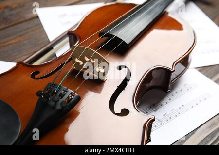 Beautiful violin, bow and note sheets on wooden table, closeup Stock Photo