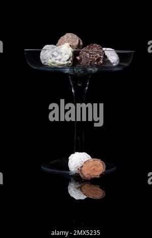 Fine truffle chocolates on a high glass bowl. On reflective black background and black background Stock Photo