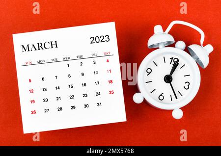 March 2023 Monthly calendar year with alarm clock on red background. Stock Photo