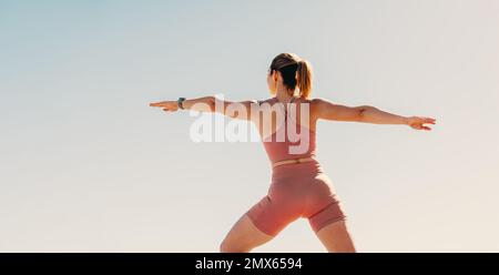 Woman practicing the warrior yoga pose outdoors. Active sportswoman practicing yoga against the sky. Virabhadrasana 2 for strength, flexibility and ba Stock Photo