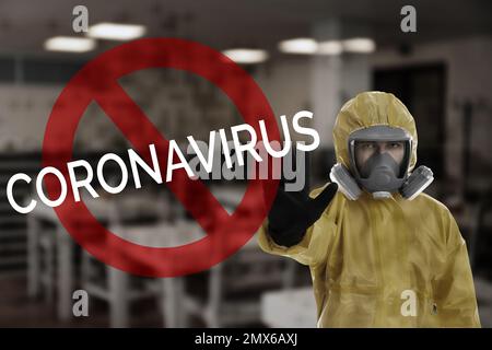 Man in chemical protective suit showing STOP gesture indoors. Prevention of virus spread Stock Photo