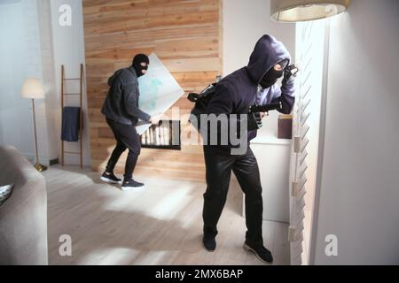 Dangerous masked criminals stealing picture from house Stock Photo