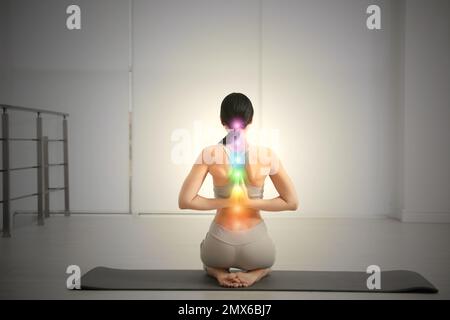 Young woman with chakra points practicing yoga in studio, back view. Healing energy Stock Photo