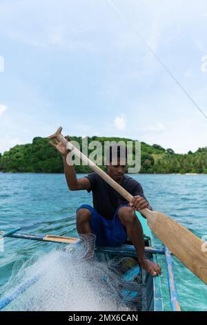 vertical photo Filipino fisherman rows on a small boat going fishing with fishing net on a tropical island. real people Stock Photo