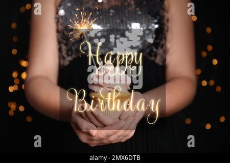 Woman holding tasty cupcake with sparkler on blurred background, closeup. Happy Birthday greetings Stock Photo