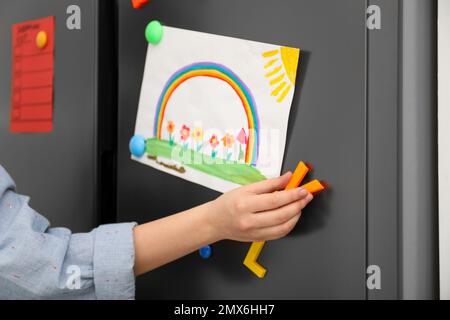 Woman putting child's drawing on refrigerator door, closeup Stock Photo