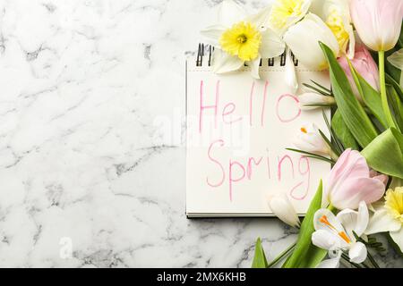 Notebook with words HELLO SPRING and fresh flowers on white marble table, flat lay. Space for text Stock Photo