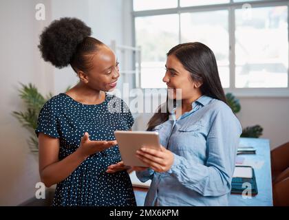 Two women discuss work solutions in boardroom office with tablet, smiling Stock Photo
