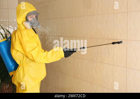 Pest control worker spraying pesticide on wall indoors Stock Photo