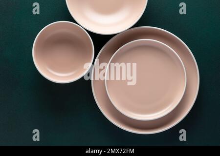 Three empty beige plates on a dark green table, grunge background. Top view. Card or menu template, flat lay, minimalistic design. Tableware, crockery Stock Photo