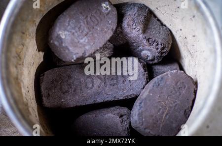 PRODUCTION - 26 January 2023, Mecklenburg-Western Pomerania, Teplitz: Coal briquettes for heating are in a bucket next to a stove. Photo: Jens Büttner/dpa Stock Photo