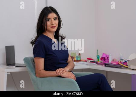Young Mexican doctor, sitting at the desk of her office, looking at the camera, with copy space. Stock Photo