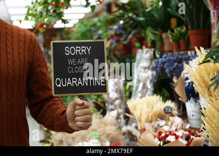 Business owner holding sign with text SORRY WE ARE CLOSED QUARANTINE in flower shop, closeup Stock Photo