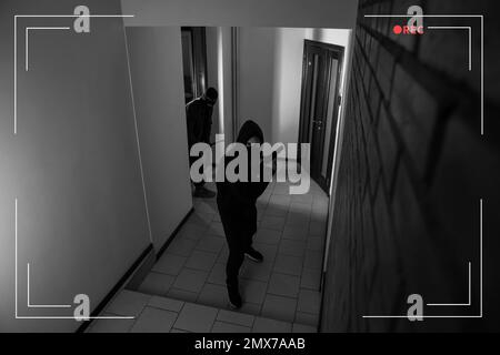 Dangerous criminals in masks with weapon in hallway, view through CCTV camera Stock Photo