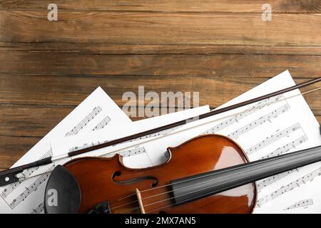 Beautiful violin, bow and note sheets on wooden table, flat lay. Space for text Stock Photo