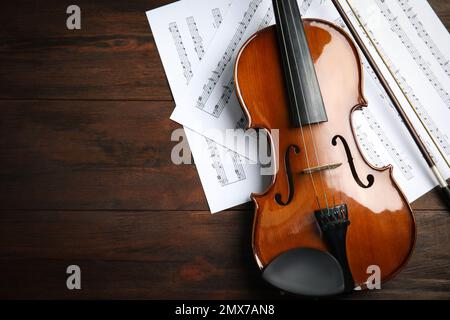 Beautiful violin, bow and note sheets on wooden table, flat lay. Space for text Stock Photo