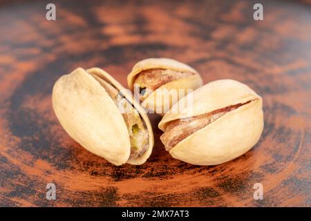 Three unshelled pistachios in a clay plate, close-up. Stock Photo