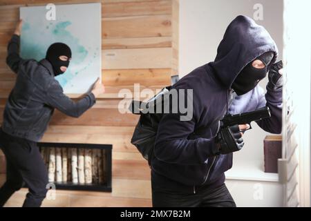 Dangerous masked criminals stealing picture from house Stock Photo