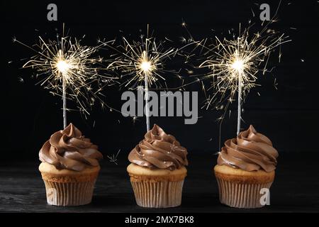 Birthday cupcakes with sparklers on table against dark background Stock Photo