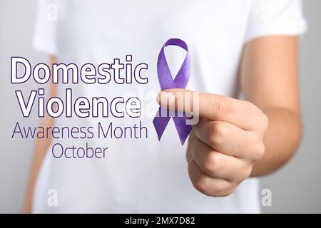 Woman holding purple ribbon on grey background, closeup. Symbol of Domestic Violence Awareness Stock Photo
