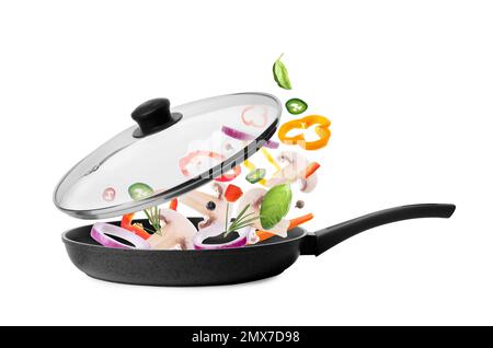 Different vegetables falling into frying pan on white background. Process of cooking Stock Photo