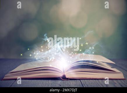 Open book with magic glowing on wooden table. Fairy tale Stock Photo
