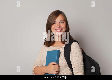 Pretty smiling joyfully brunette female dressed casually, looking with satisfaction at camera, being happ isolated against grey studio wall. Stock Photo