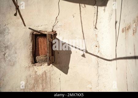 Whitewashed and aged white wall with a small wooden window and shutter with play of shadows on the wall Stock Photo