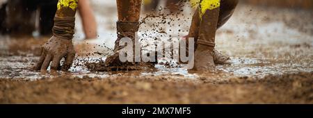 Mud race runners. Crawling,passing under a barbed wire obstacles during extreme obstacle race Stock Photo