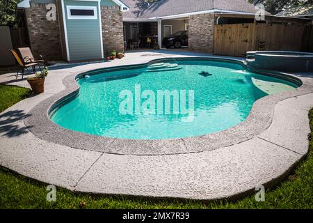 A large free form gray grey accent swimming pool with turquoise blue water in a fenced in backyard Stock Photo