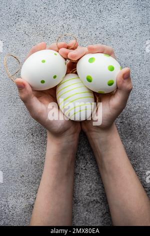 From above cropped unrecognizable kid with hands full with stripped and dot's eggs on grey concrete background Stock Photo