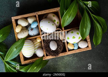 From above spring Easter wooden box with colored eggs and nest surrounded by italian Ruscus plant Stock Photo
